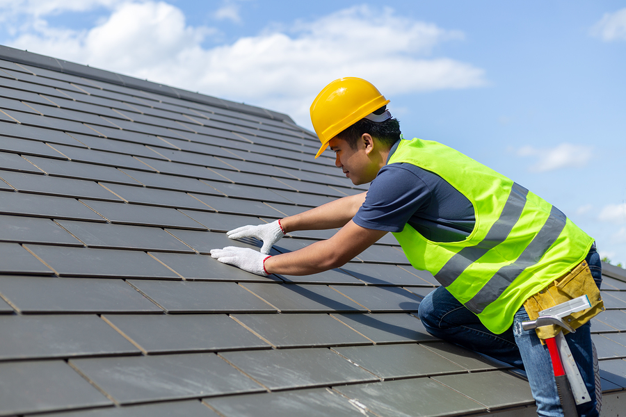 worker with white gloves replacing gray tiles or shingles on house with blue sky as background and copy space