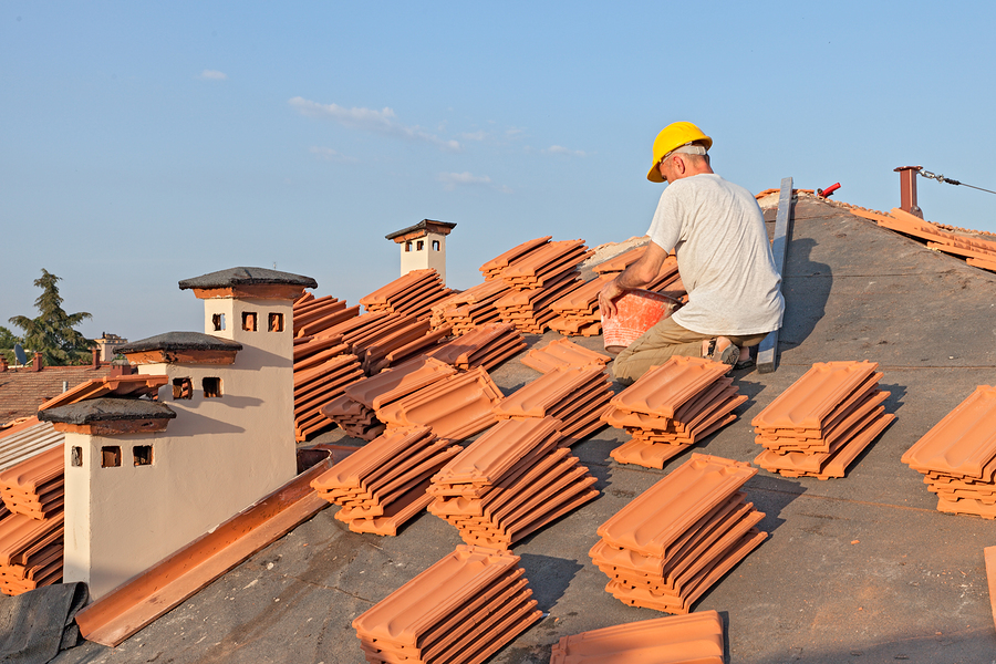 construction worker on a roof covering it with tiles